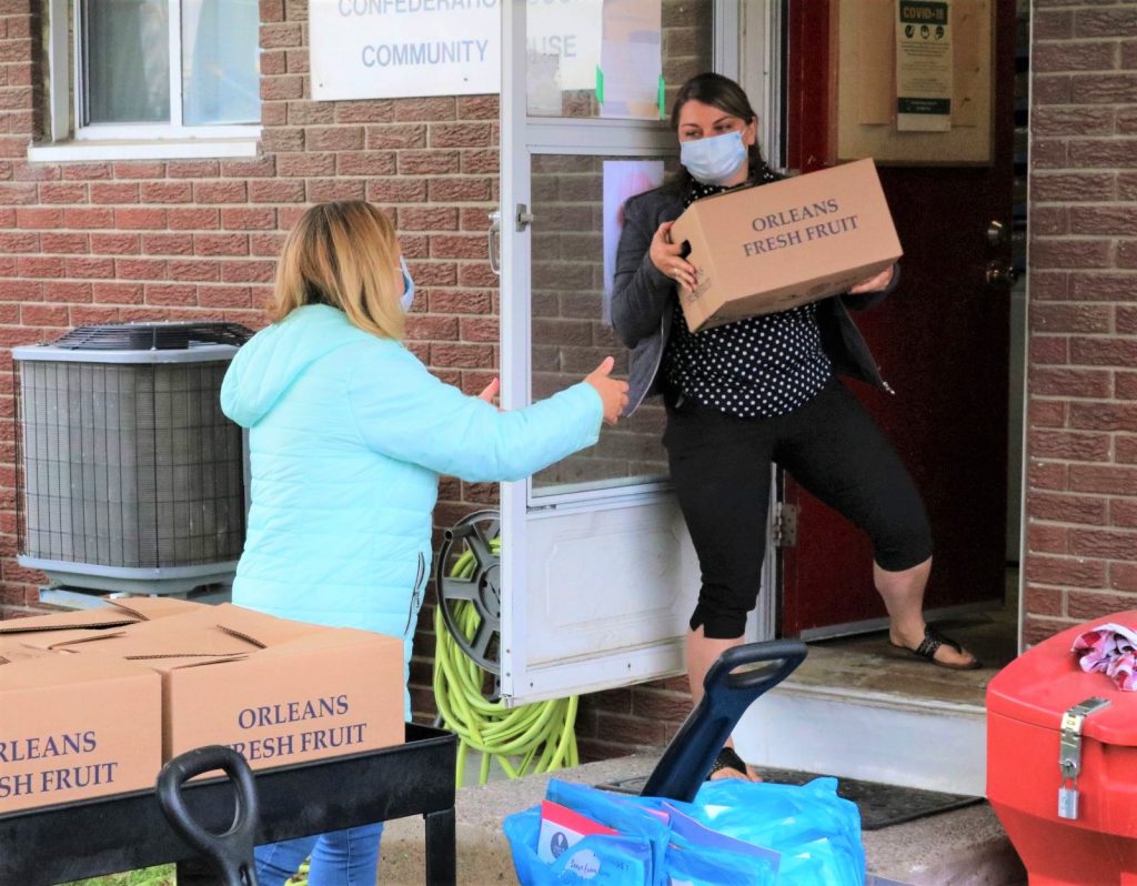 Woman in mask passes box of food to her colleague