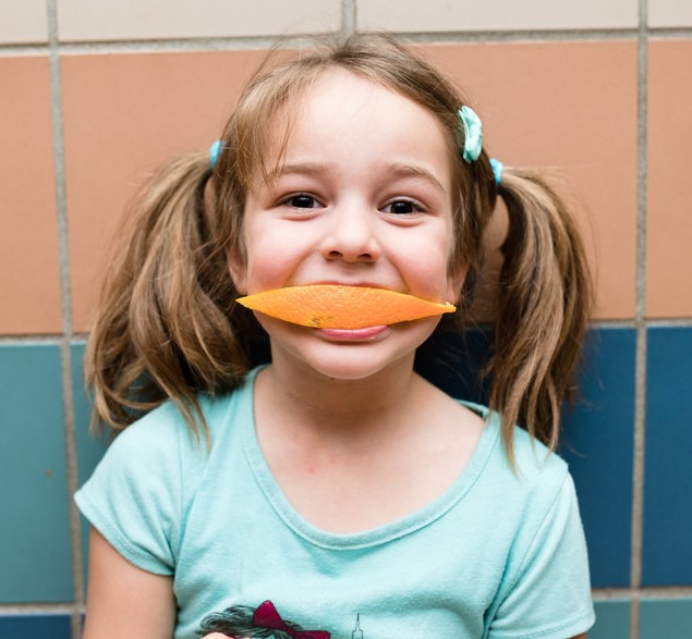 Girl smiling with orange slice in her mouth