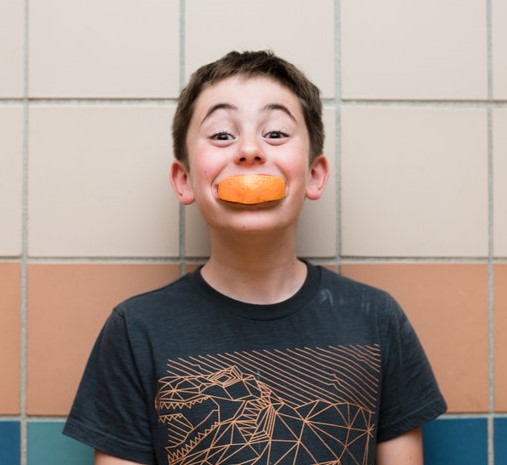 Boy smiling with orange slice in his mouth
